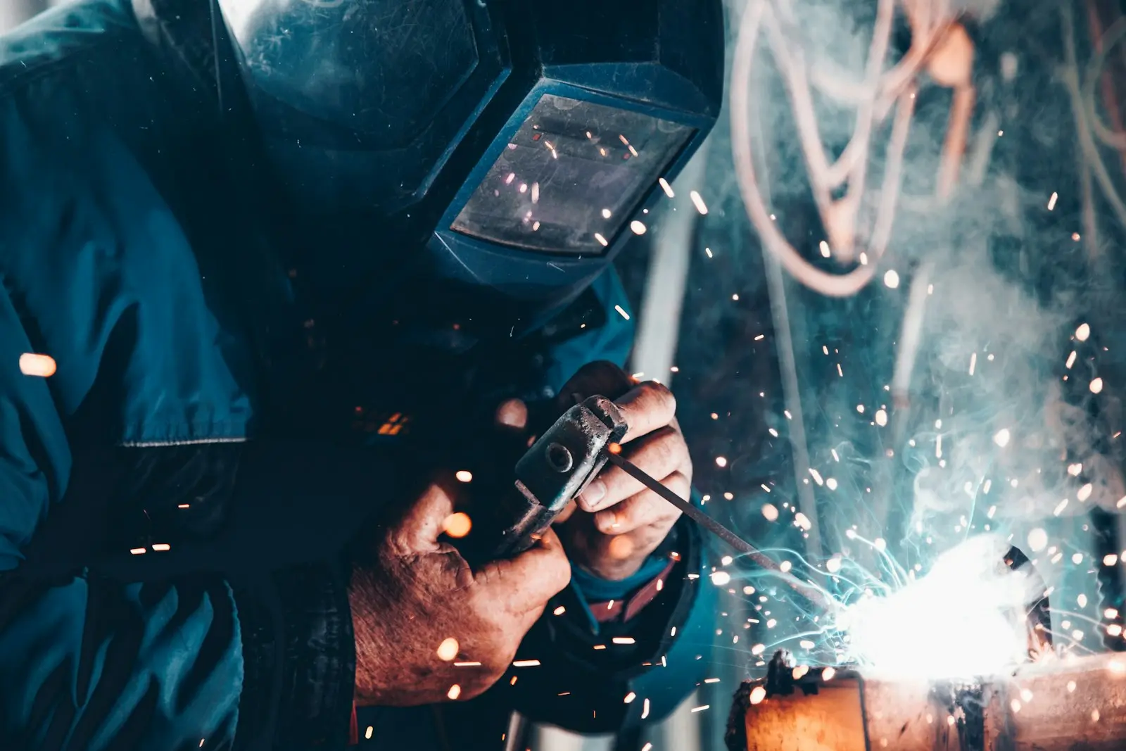 Soldador trabajando en una fábrica, con chispas de soldadura en primer plano